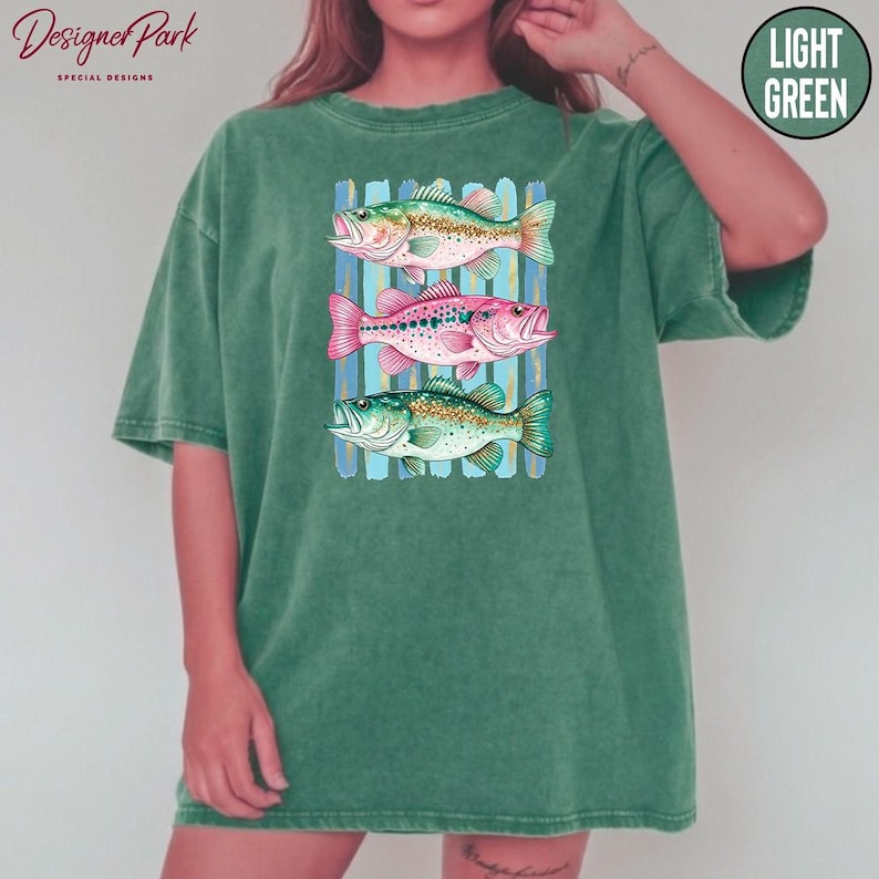 A person wearing a green t-shirt with a graphic design of three colorful fish swimming in a row.