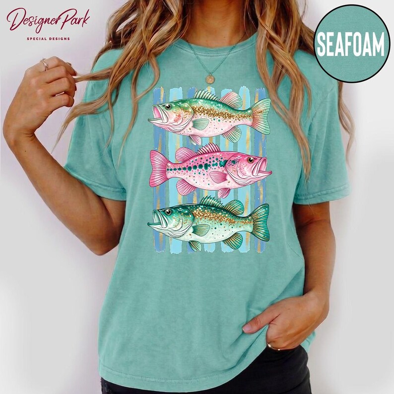 A woman wearing a teal t-shirt with a graphic of three colorful fish.
