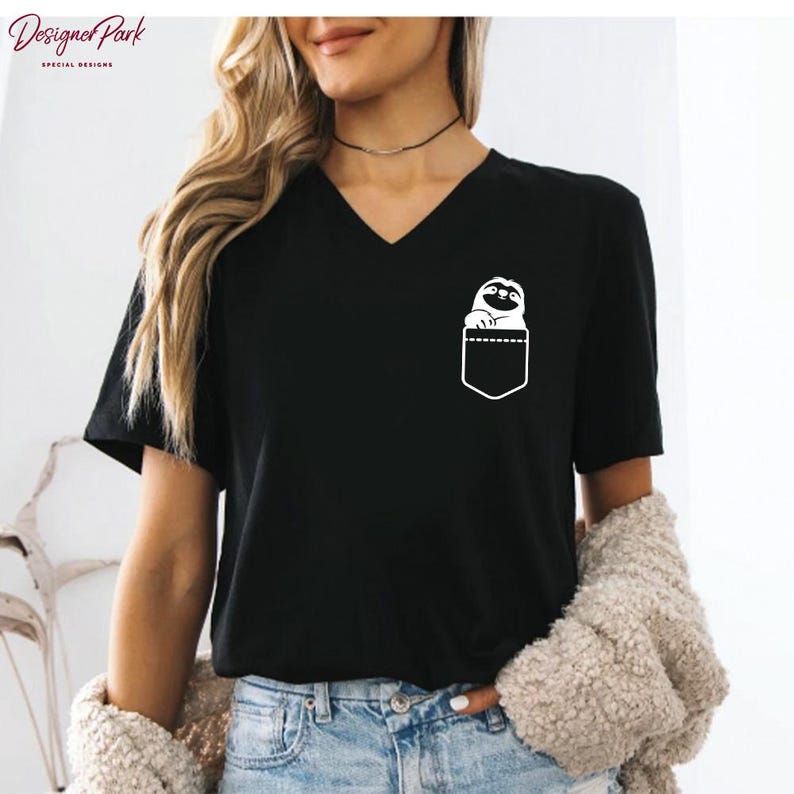 Puede incluir: Camiseta negra con cuello en V con un dise&ntilde;o gr&aacute;fico blanco de un perezoso asomando por un bolsillo. La camiseta tiene mangas cortas y un corte relajado. La marca "Designer Park Special Designs" est&aacute; impresa en la esquina superior izquierda.