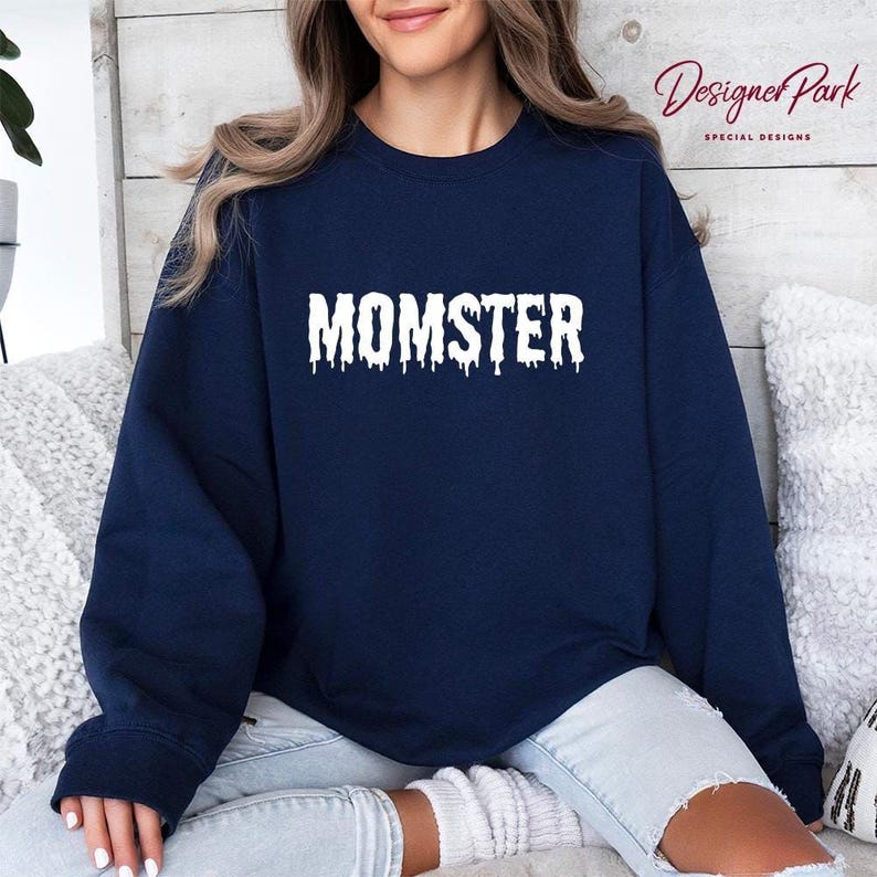 A woman wearing a navy blue sweatshirt with the word "MOMSTER" printed on it, sitting on a couch.