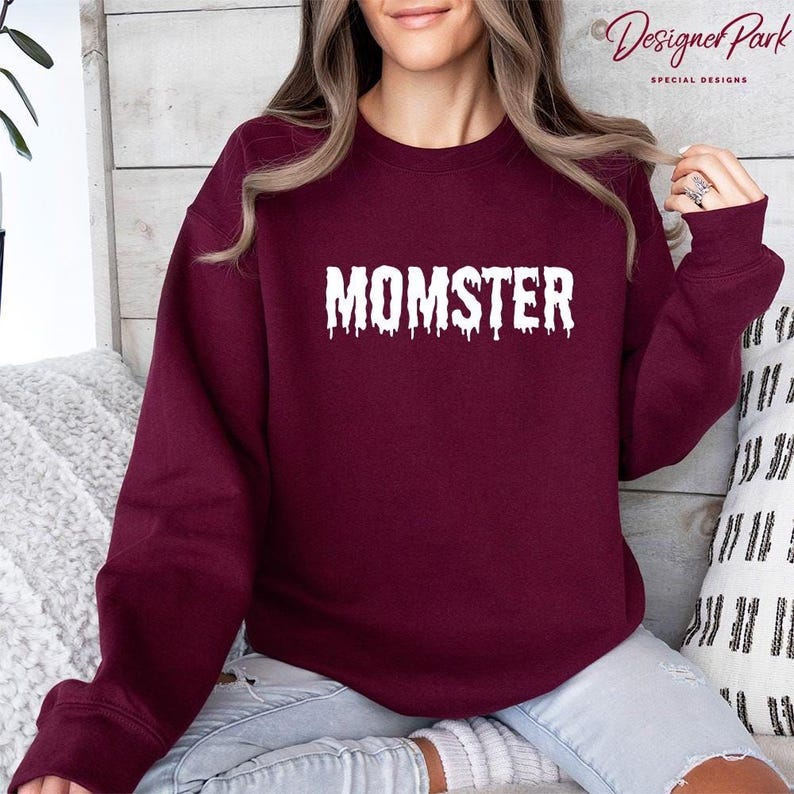 A woman wearing a burgundy sweatshirt with the word "MOMSTER" printed on it.