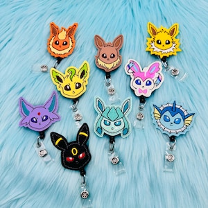 K&ouml;nnte beinhalten: Acht bunte, gestickte Pok&eacute;mon-Charakter-Badge-Rollen mit einziehbaren Schn&uuml;ren. Die Charaktere sind Eevee, Flareon, Jolteon, Vaporeon, Espeon, Umbreon, Glaceon und Leafeon.