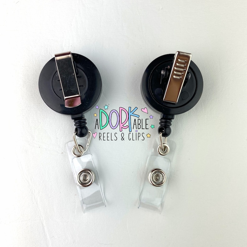 May include: Two black retractable badge reels with silver clips and clear plastic badge holders. The reels have the text "A DORK ABLE REELS & CLIPS" in a colorful, whimsical font.