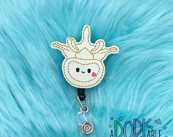 May include: White embroidered cartoon of a human spinal cord with a cute face and a pink heart. The cartoon is attached to a clear plastic retractable badge holder with a black clip.