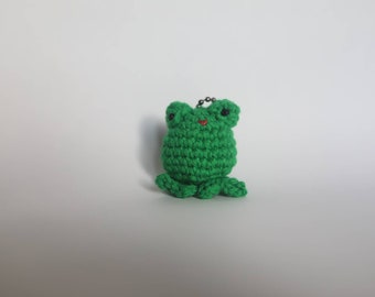 May include: A green crocheted frog keychain with black eyes and a red mouth.