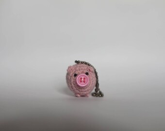 May include: A pink crocheted pig keychain with a pink button nose and black eyes.