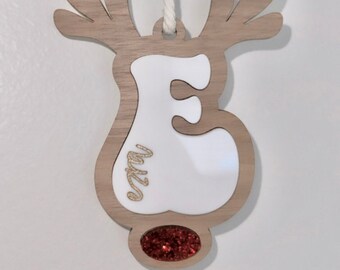 May include: Wooden reindeer Christmas ornament with a white letter "E" in the center and gold glitter accents. The bottom section is filled with red glitter. A cream-colored string is attached for hanging.