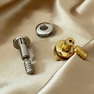 May include: Two metal hardware pieces, one silver and one gold. The silver piece is a small, round, flat washer with a hole in the centre. The gold piece is a small, round, flat washer with a hole in the centre and a small, gold, metal knob attached to the side.
