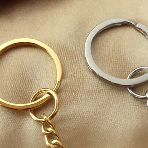 以下が含まれることがあります： 金と銀のキーホルダーが2つあり、それぞれにチェーンが付いています。キーホルダーはどちらも円形で、滑らかな仕上がりです。