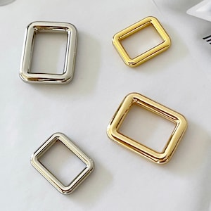 May include: Four rectangular metal buckles in gold and silver tones. The buckles have rounded corners and a smooth, polished finish. The buckles are likely for use in bag making or other craft projects.