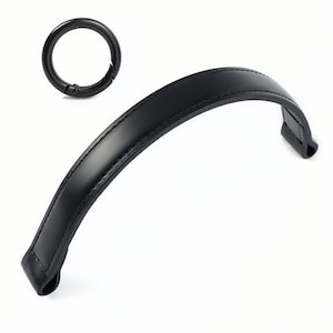 Puede incluir: Asa de cuero negro con una costura. El asa es curva y tiene un lazo de metal en un extremo.