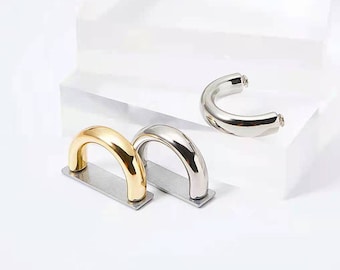 May include: Three metal hoops in gold and silver. The hoops are curved and have a smooth, polished finish.