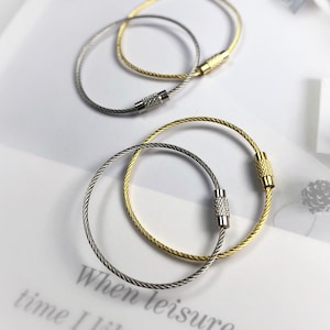 May include: Three key rings made of silver and gold metal cable. The key rings are in the shape of a circle and have a small metal clasp.