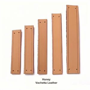 Peut inclure: Cinq bandes rectangulaires en cuir vachette couleur miel dispos&eacute;es par longueur croissante. Chaque bande pr&eacute;sente deux lignes verticales en relief et deux trous pr&eacute;-perc&eacute;s aux extr&eacute;mit&eacute;s. Le texte indique Honey Vachetta Leather.