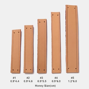 Peut inclure: Cinq lani&egrave;res en cuir beige rectangulaires avec des bords cousus et deux trous pr&eacute;-perc&eacute;s &agrave; chaque extr&eacute;mit&eacute;. Les lani&egrave;res sont &eacute;tiquet&eacute;es #1 &agrave; #5 avec des dimensions en centim&egrave;tres : 0,9x4,4, 0,9x4,8, 0,9x5,5, 0,9x6,0 et 1,2x6,8. Texte : Honey Size(cm).