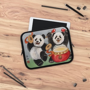 May include: A black and white tablet sleeve featuring two pandas playing musical instruments. The pandas are depicted with expressive faces and are surrounded by musical instruments in shades of red and gold. The sleeve is on a wooden surface.