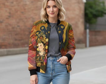Puede incluir: Chaqueta bomber colorida con una ilustración ornamentada de una mujer con un tocado y joyas detalladas. La chaqueta tiene cuello, puños y dobladillo negros. El diseño incorpora tonos dorados, rojos, azules y verdes.