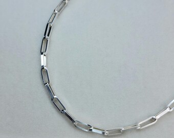 Può includere: Una collana a catena color argento con un design a maglie rettangolari. La collana è presentata su uno sfondo grigio chiaro. Le maglie sono uniformi per dimensioni e forma, creando un aspetto elegante e moderno. Questo gioiello è adatto all'uso quotidiano.