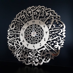 Może przedstawiać: Srebrny zegar lustrzany z arabską kaligrafią otaczającą tarczę zegara. Tarcza zegara ma geometryczny wzór i cyfry rzymskie.