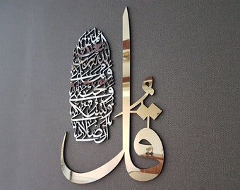 May include: A gold-colored metal wall art piece featuring intricate Arabic calligraphy. The design is a combination of a vertical line and a curved shape, with the calligraphy filling the space between them.