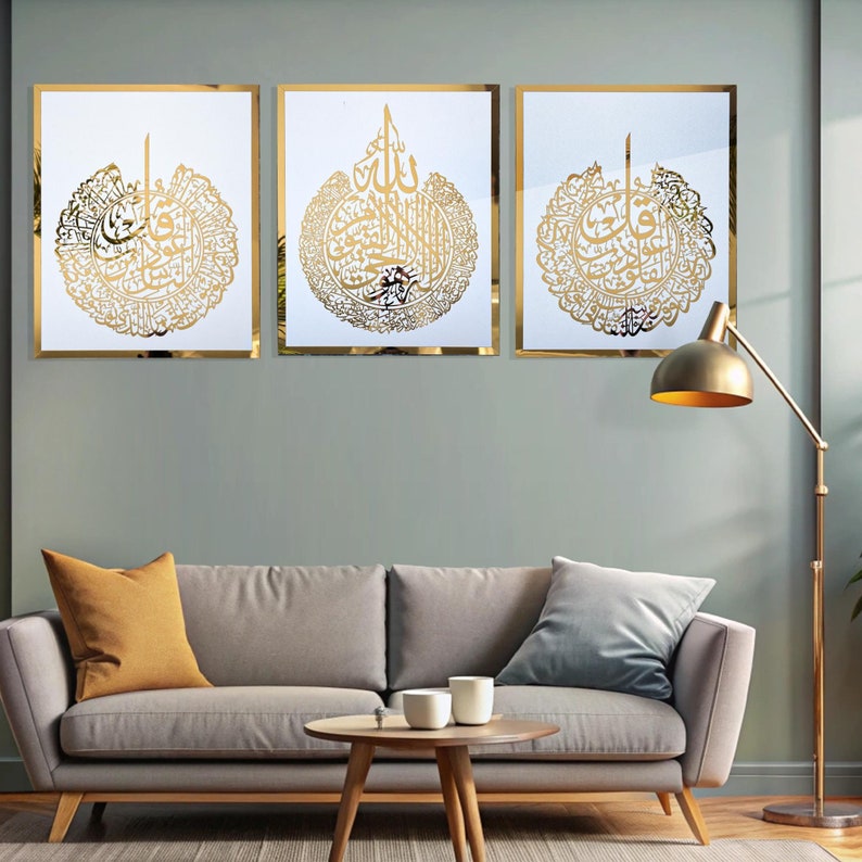 May include: Three framed wall art pieces with gold calligraphy on a white background. The calligraphy is in a circular design with intricate details. The frames are gold, and the artwork is displayed above a gray sofa with decorative pillows.