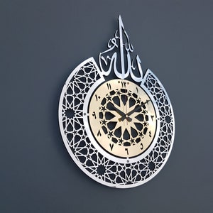 May include: A silver and gold wall clock with an intricate geometric design and Arabic calligraphy. The clock face features a gold background with black Roman numerals and a black star pattern.