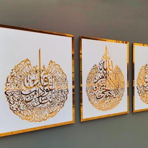 May include: Three framed art pieces with gold calligraphy on a white background. The gold frames and calligraphy create a luxurious look. The artwork is displayed on a gray wall.