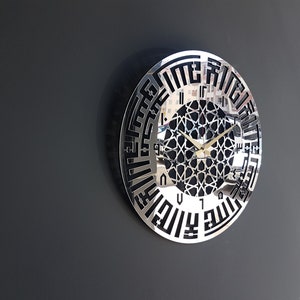 May include: A silver and black wall clock with Arabic numerals and a geometric design in the center. The clock hands are gold.