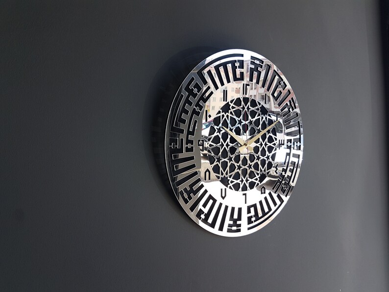 May include: A silver and black wall clock with Arabic numerals and a geometric design in the center. The clock hands are gold.