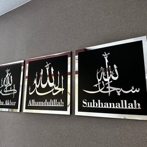 May include: Three black framed wall decor pieces with silver lettering. The lettering is in Arabic script and translates to "Allahu Akbar", "Alhamdulillah", and "Subhanallah".