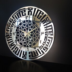 May include: A silver mirrored clock with black Arabic numerals and a black geometric design in the center. The clock hands are gold.