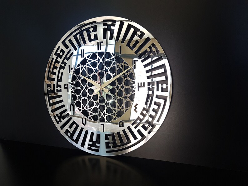 May include: A silver mirrored clock with black Arabic numerals and a black geometric design in the center. The clock hands are gold.