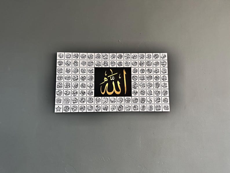 Puede incluir: Arte mural rectangular con caligraf&iacute;a dorada de la palabra "Allah" sobre un fondo negro. La obra de arte est&aacute; enmarcada por una cuadr&iacute;cula de peque&ntilde;os cuadrados de escritura &aacute;rabe en blanco y negro. Se exhibe contra una pared gris.