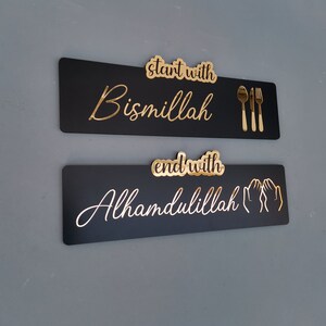 May include: Two black rectangular signs with gold lettering. The top sign says "start with Bismillah" and has a gold fork, knife, and spoon. The bottom sign says "end with Alhamdulillah" and has two gold hands in a praying position.