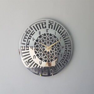May include: A silver mirrored clock with Arabic numerals and a geometric design in the center. The clock hands are gold.