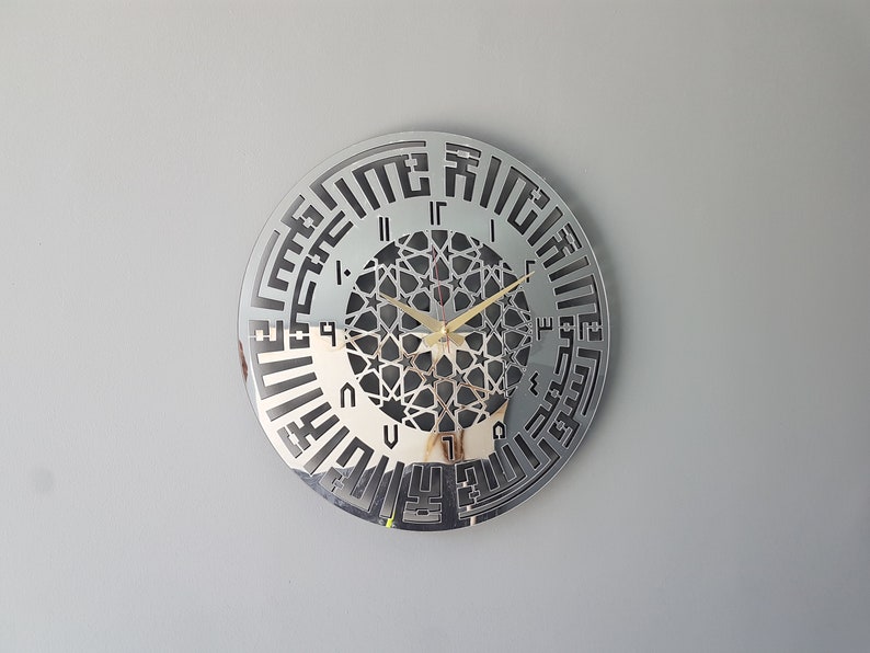 May include: A silver mirrored clock with Arabic numerals and a geometric design in the center. The clock hands are gold.