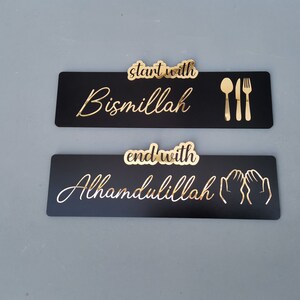 May include: Two black rectangular signs with gold lettering. The top sign says "start with Bismillah" and has a gold fork, knife, and spoon. The bottom sign says "end with Alhamdulillah" and has two gold hands in a praying position.