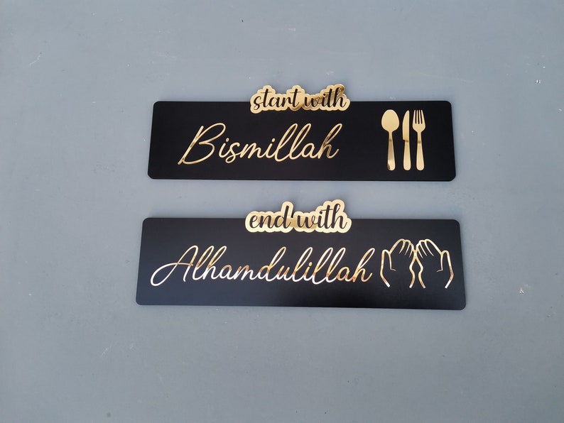 May include: Two black rectangular signs with gold lettering. The top sign says "start with Bismillah" and has a gold fork, knife, and spoon. The bottom sign says "end with Alhamdulillah" and has two gold hands in a praying position.