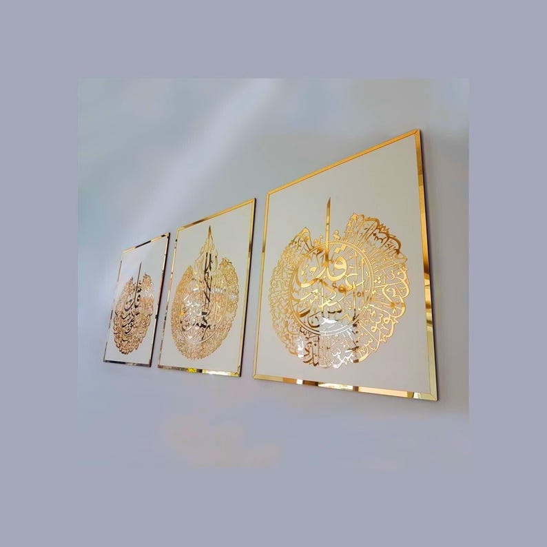 May include: Three framed wall art pieces with gold calligraphy on a cream background. The gold frames and calligraphy create a luxurious aesthetic. The artwork is displayed on a white wall.