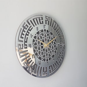 May include: A silver mirrored wall clock with Arabic numerals and a geometric design in the center. The clock hands are gold.