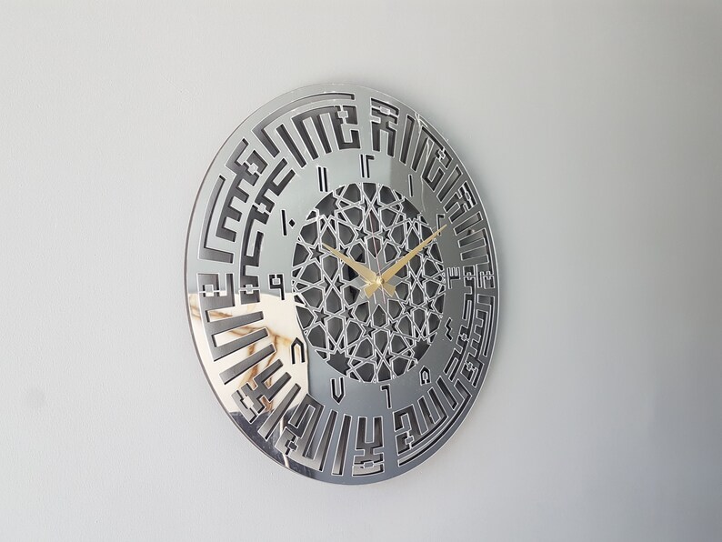 May include: A silver mirrored wall clock with Arabic numerals and a geometric design in the center. The clock hands are gold.