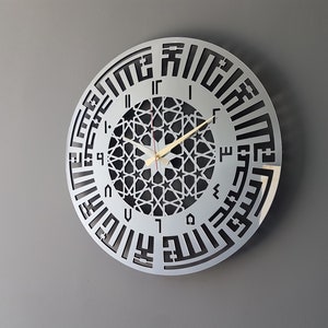 May include: A silver round clock with black Arabic numerals and a geometric design in the center. The clock hands are gold.