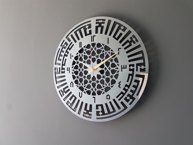 May include: A silver round clock with black Arabic numerals and a geometric design in the center. The clock hands are gold.