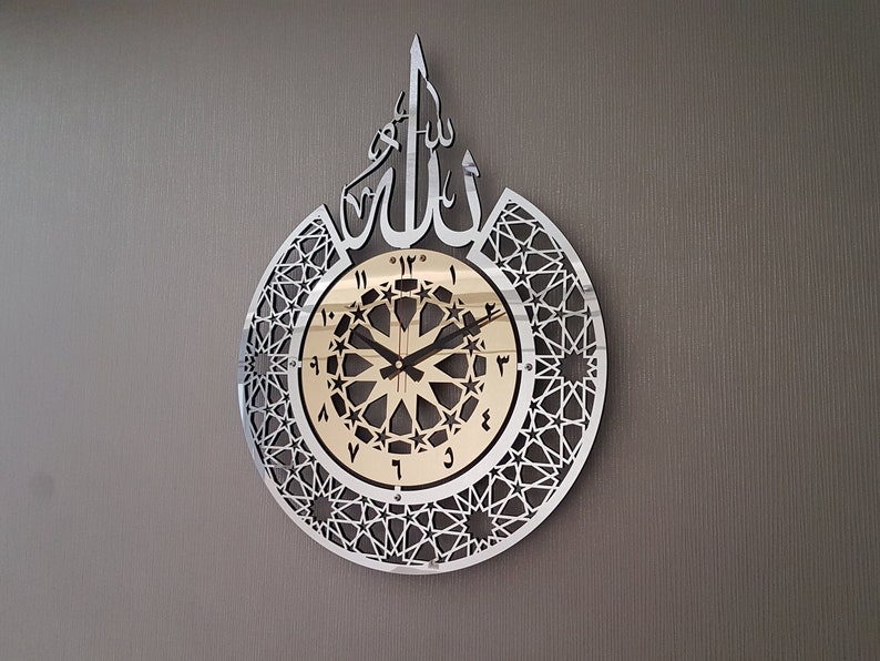 May include: A silver and gold wall clock with Arabic numerals and a geometric design. The clock features the word "Allah" in Arabic script.