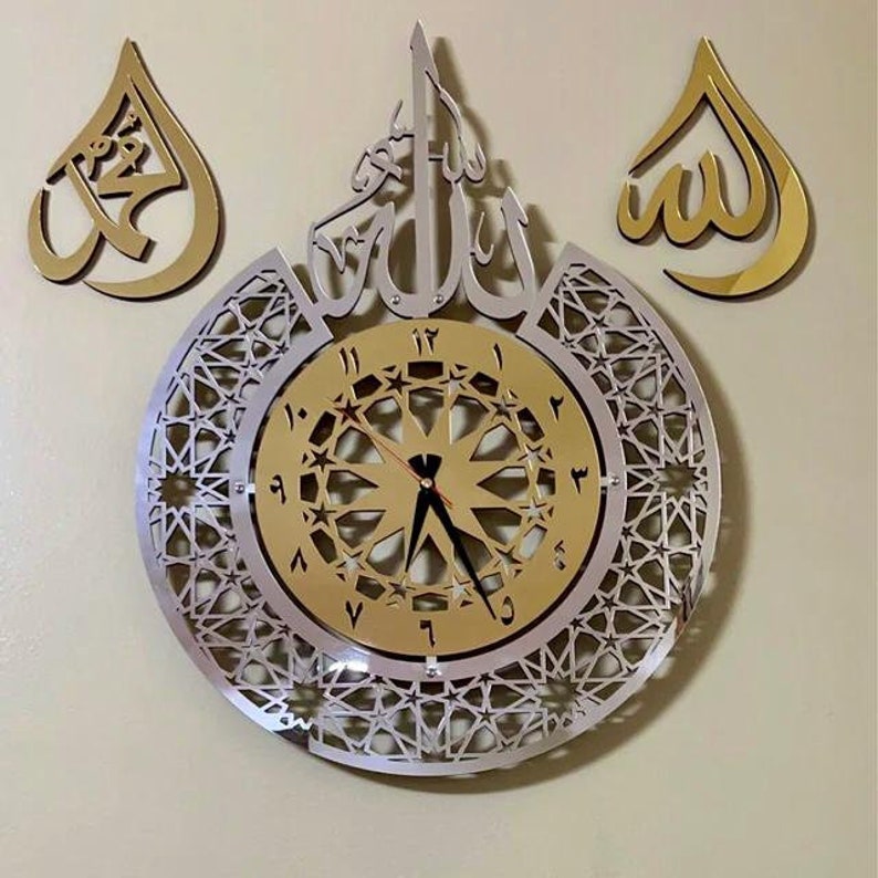 May include: A gold and silver wall clock with Arabic calligraphy and a geometric design. The clock face features Roman numerals and a starburst pattern.