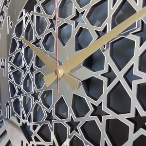 May include: A silver clock face with a geometric pattern of stars and a gold and red hour and minute hand.