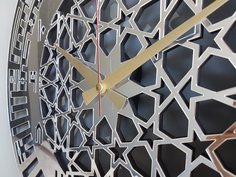 May include: A silver clock face with a geometric pattern of stars and a gold and red hour and minute hand.