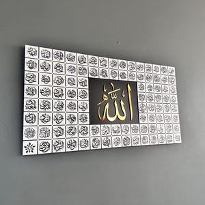 Puede incluir: Arte mural rectangular con caligraf&iacute;a &aacute;rabe. La obra presenta un fondo blanco con escritura negra dispuesta en un patr&oacute;n de cuadr&iacute;cula. El panel central es negro con texto &aacute;rabe dorado. La palabra "Allah" se muestra de forma destacada.