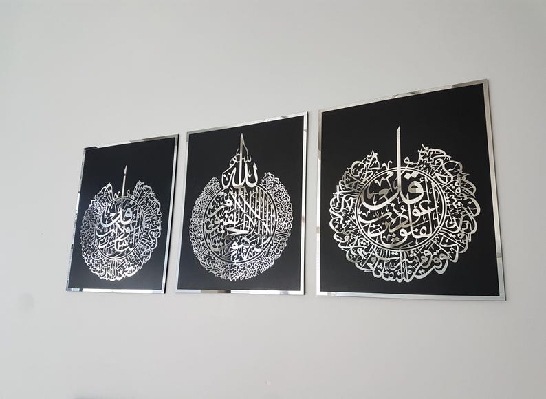 May include: Three framed wall art pieces with intricate silver calligraphy on a black background. The artwork is displayed on a white wall. Each piece has a silver frame, adding a touch of elegance to the Islamic art.