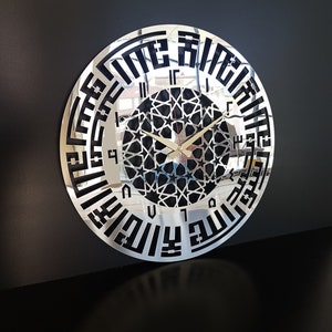 May include: A silver mirrored wall clock with black Arabic numerals and a black geometric design in the center. The clock has a reflective surface.